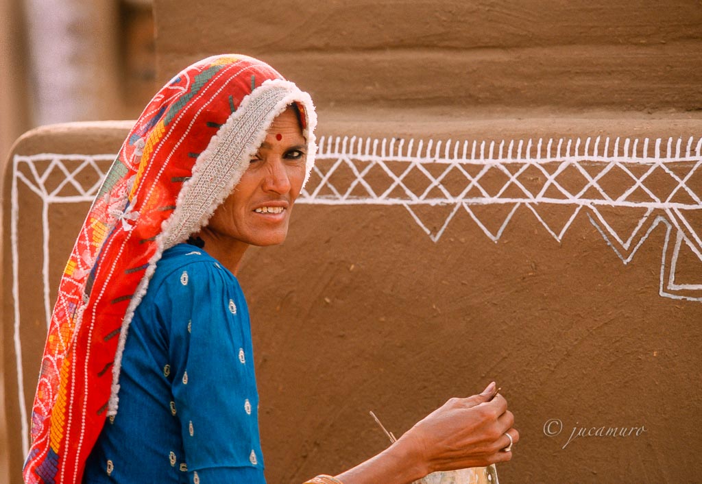 Woman with typical attire decorating adobe houses. Rajasthan. India.